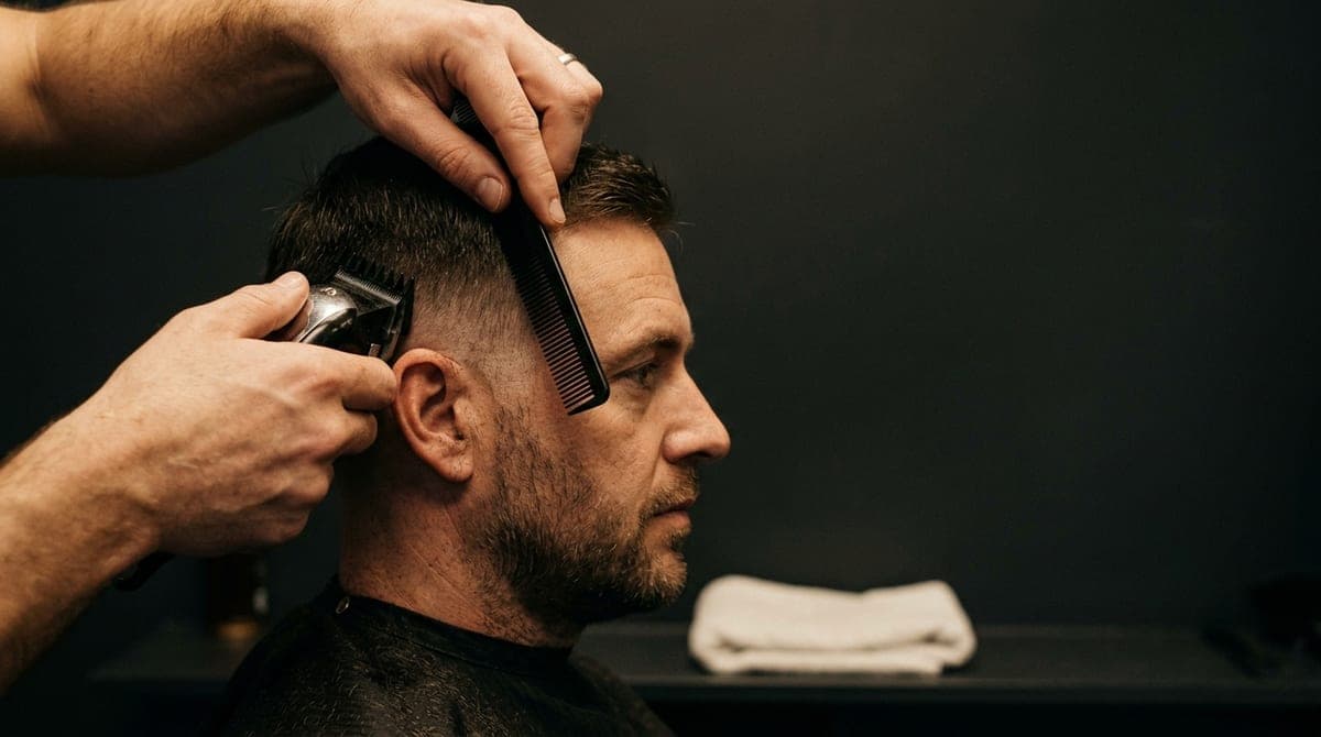 Close view of a barber blending clipper work above the ear on a short fade